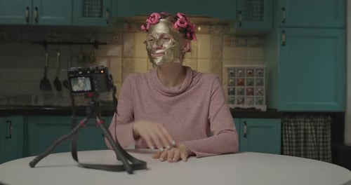 Mujer joven de 30 años grabando un divertido Vídeo de la aplicación de una máscara cosmética facial en casa. Bloguera femenina divertida