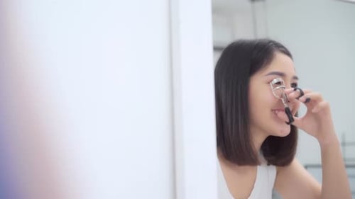 Young Woman Using Eyelash Curler in Bathroom