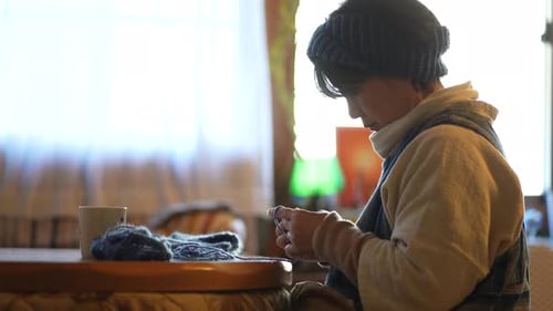 Woman Knitting with Yarn at Table in Home