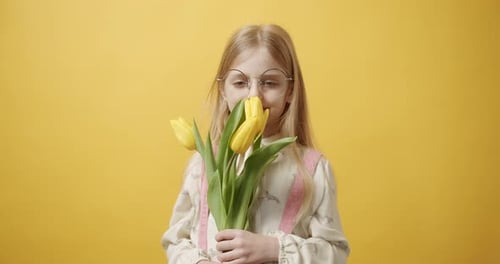 Happy Girl Smelling Yellow Tulips on Yellow Background