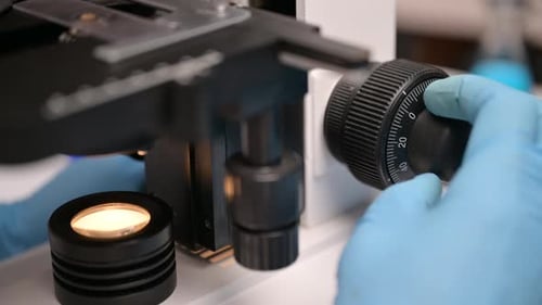 Gloved Hand Adjusting Microscope Focus Knob