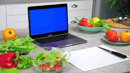 Blue Screen Laptop on Kitchen Table Near Vegetables and Cutting Board with Knife