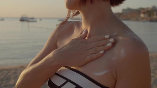 Woman Applying Sunscreen on Her Neck Standing on the Beach