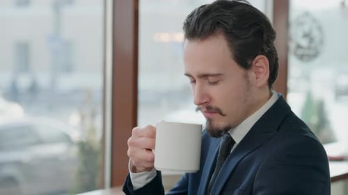 Young Man Drinking Coffee by Cafe Window
