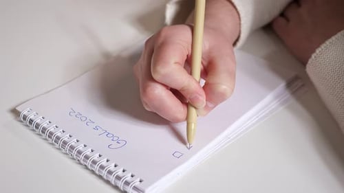 Closeup of Female Hands Writing Goals for 2022 By Pen on Paper