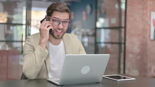 Young Adult Man Using Phone and Laptop in Office