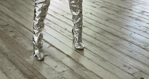 Woman Wears Sparkling Silver Boots on Wooden Floor