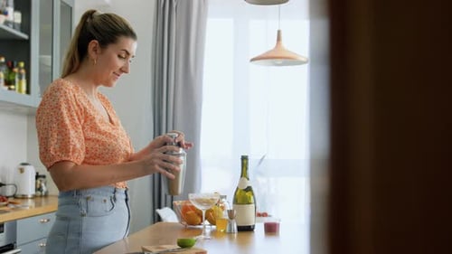 Woman with Shaker Pouring Cocktail Drink to Glass