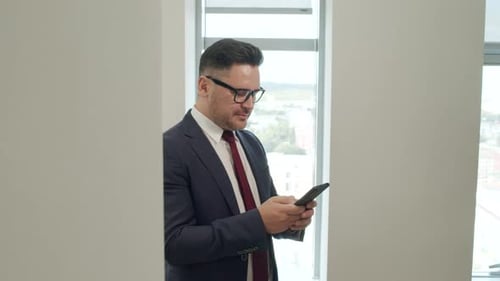 Happy Businessman Uses Smartphone in Bright Office