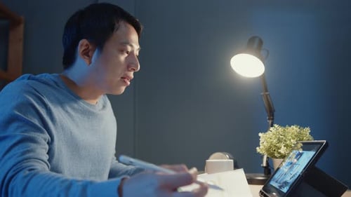 Asia freelance businessman video call meeting on tablet computer assignment paperwork.