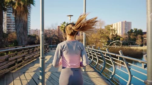 Back View Millennial Sportswoman Wearing Earphones Running By Bridge