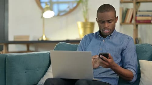 Young Adult Uses Smartphone and Laptop at Home