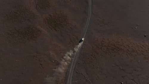 High Angle Footage of Fast Moving Car on Dusty Dirt Road in Volcanic Wasteland