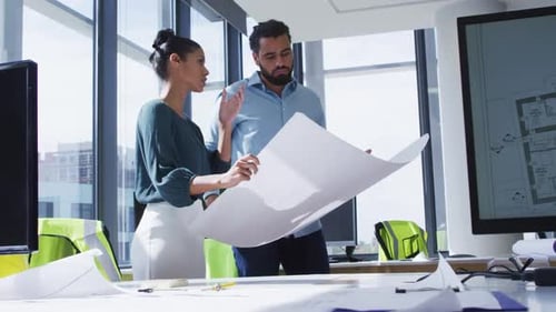 Two diverse male and female colleagues holding architectural blueprint and discussing