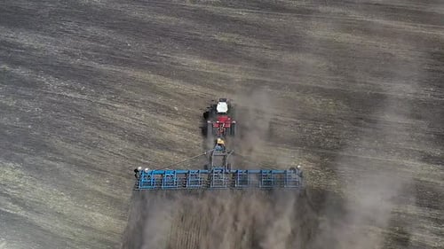 Red Tractor Cultivating Brown Earth in Sunny Spring Weather