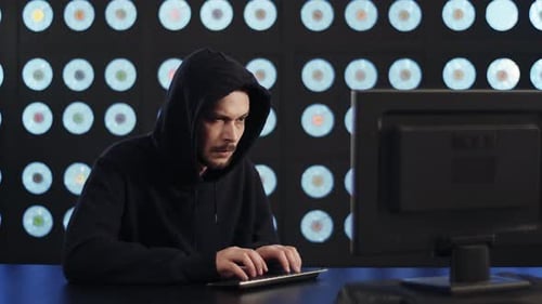 Bärtiger reifer Kerl Computerhacker trägt schwarzen Hoodie arbeitet im dunklen Raum
