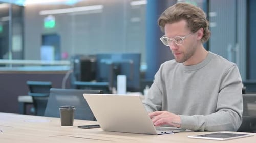Young Businessman with Laptop Thinking at Work
