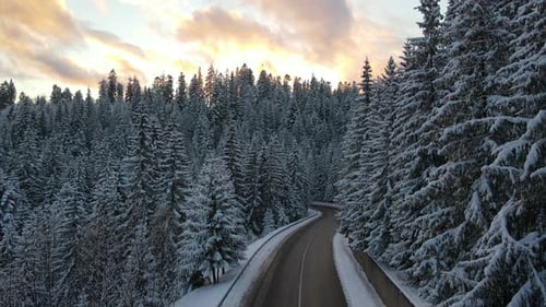 Aerial view of winter landscape with snow covered mountain hills and winding forest road in morning.