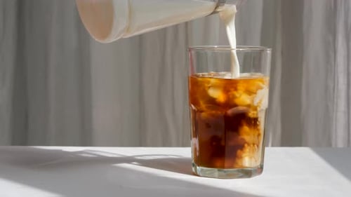 Milk Poured into Iced Coffee in a Glass