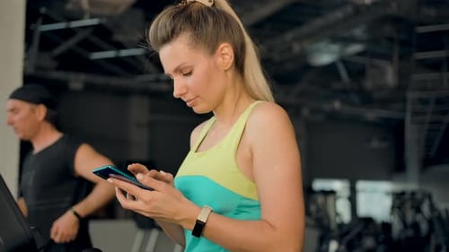 Woman Using Treadmill and Smartphone in Gym