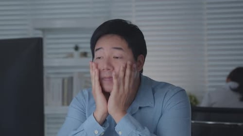 Tired Asian Male Worker Working on desktop computer in the Corporate Office,