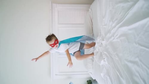 Energetic Boy Superhero Jumps on Bed Indoors