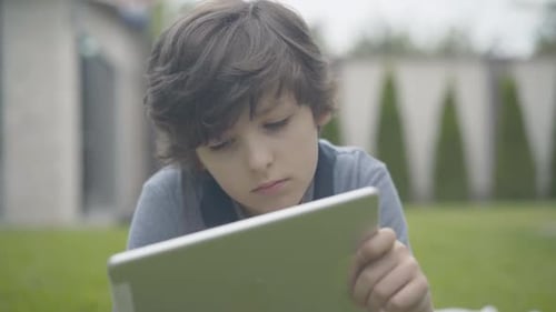Close-up Portrait of Lonely Boy Using Tablet Outdoors. Unhappy Caucasian Schoolboy Spending Weekends