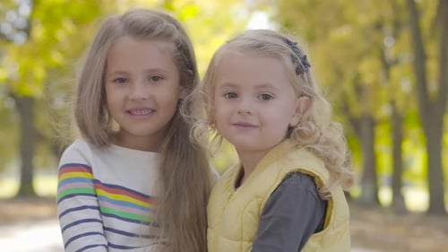 Two Pretty Little Caucasian Sisters Standing in the Autumn Park and Smiling