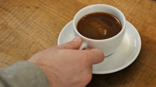 Person's hand removes a coffee cup from a saucer