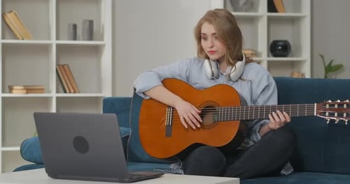 Woman Plays Guitar at Home While Watching Laptop