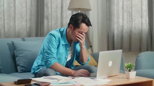 Asian Man Being Worried While Typing On A Laptop At Home