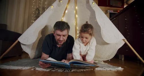 Dad and Daughter Reading Book in Tent at Home