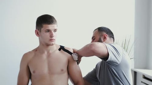 Osteopath Doing Kinesiology Taping on Patient's Shoulder in Clinic