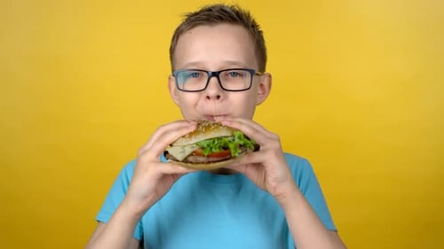 Child Eating Burger in Front of Yellow Backdrop
