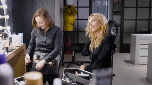 Professioneller Meister des Make-ups trägt Lippenstift auf die Lippen einer blonden Frau im Schönheitsstudio auf