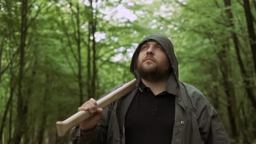 Porträt eines positiven Holzfällers, der mit Pro Axt im wilden Laubwald spaziert.