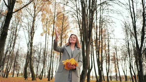 A Young Girl Throws Up Leaves in an Autumn Park.