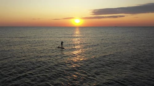 Mujer joven en una tabla de surf de remo haciendo ejercicio al atardecer. Tabla de stand up paddle