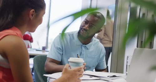 Diverse male and female business colleagues talking and taking notes in office