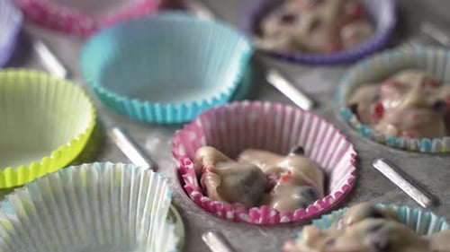 Scooping muffin batter with tasty fruit into colorful wrappers in metal baking tray close up