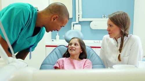 Friendly dentist and her assistant talking with lovely little girl