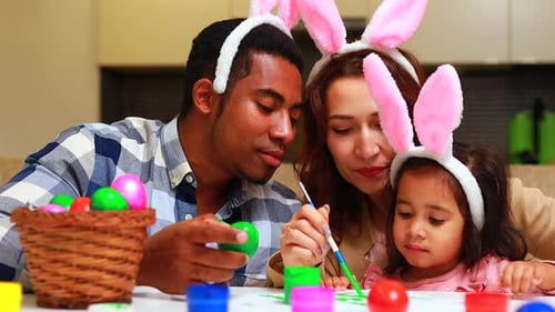 Multikulturelles süßes kleines Kind Mädchen trägt Hasenohren am Ostertag Eier bemalen in der Küche mit