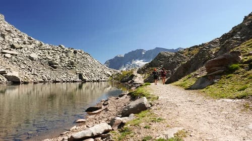 Couple hiking on mountain top in high altitude rocky landscape and alpine lake