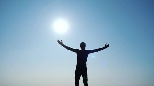 Young Long-haired Inspired Man Raises His Hands Up Standing on the Top of a Mountain Above the Sea