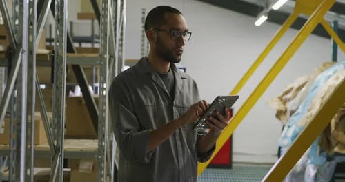 Afroamerikanischer Automechaniker steht in einem Lagerhaus und benutzt ein Tablet
