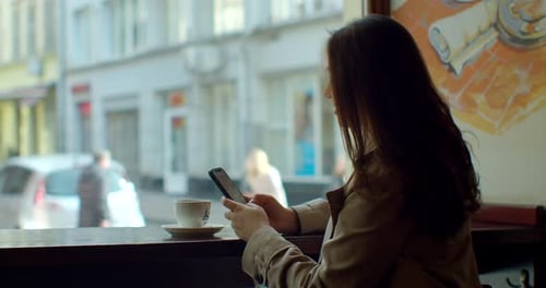 Young Woman Using Smartphone Drinking Coffee in Cafe Texting Sharing Messages on Social Media