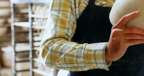 Craftsman Inspecting Pottery in Bright Workshop