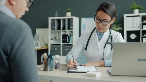 Female Doctor Talking To Elderly Man Patient in Office During Appointment in Clinic