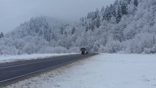 Luftaufnahme: Autos und Lastwagen fahren im Winterwald an der Straße vorbei.