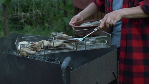 Nahaufnahme von Frauenhänden legen gekochten gegrillten Fisch auf den Teller. Familie beim Grill-Picknick im Sommerhaus